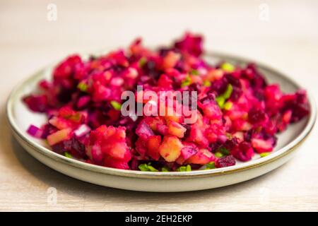 Russischer Vinegret-Rübensalat aus gekochtem Gemüse in grauem weißem Teller auf weißem Tischhintergrund. Stockfoto