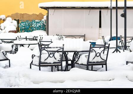 Leere Tische und Stühle vom Schnee bedeckt. Covid oder Coronavirus betrifft die globale Lebensmittelindustrie, Restaurants und Bar bankrott wegen der Krise Stockfoto