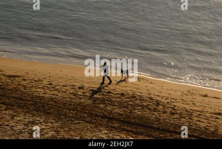 Frau, die mit einem Hund am Strand Playa de los Bikinis läuft Santander Cantabria Spanien Winter ruhiger, sonniger Morgen Stockfoto