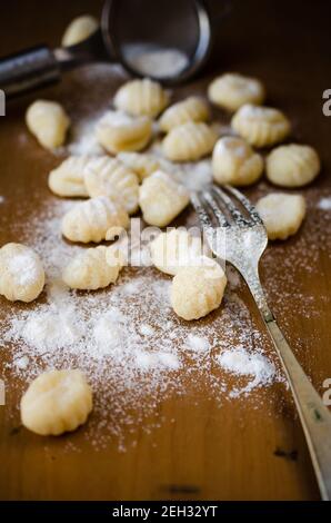 Frische hausgemachte ungekochte Gnocchi auf einem bemehlten Holzbrett mit einer Gabel und einem Sieb auf dem Hintergrund. Stockfoto