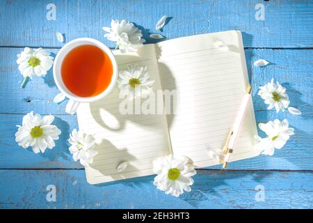 Gemütliches Frühstück im Frühjahr oder frühen Herbst Tee mit Bouquet von Kamille Gänseblümchen Blumen und Notizbuch. Platz kopieren, Draufsicht flach liegend Stockfoto