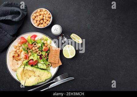 Gesunde Salatschüssel mit Avocado und Kichererbsen auf schwarzem Betonboden. Kopiespeicherplatz in der Draufsicht Stockfoto