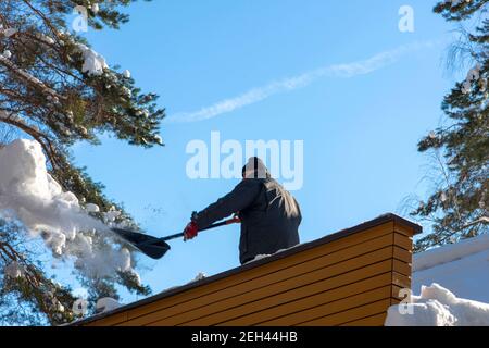 Mann, der Schnee von einem Dach mit einer Schaufel entfernt Stockfoto