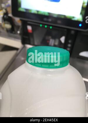 Ein Karton mit britischer halbmager pasteurisierter Milch mit einer grünen Flaschenspitze wird von einem Regal zur Kasse in einem Supermarkt transportiert. Der Kunde kauft die Milch im Laden und scannt sie an der Selbstbedienungskasse. Ein kleiner Kauf mit einer Kreditkarte; sind die Menschen mit Kartenzahlung für sehr kleine Beträge durch Lockdown und bargeldlos kommen normal. VEREINIGTES KÖNIGREICH. (123) Stockfoto