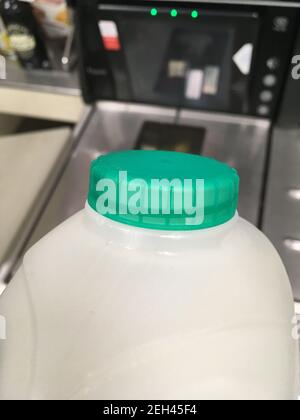 Ein Karton mit britischer halbmager pasteurisierter Milch mit einer grünen Flaschenspitze wird von einem Regal zur Kasse in einem Supermarkt transportiert. Der Kunde kauft die Milch im Laden und scannt sie an der Selbstbedienungskasse. Ein kleiner Kauf mit einer Kreditkarte; sind die Menschen mit Kartenzahlung für sehr kleine Beträge durch Lockdown und bargeldlos kommen normal. VEREINIGTES KÖNIGREICH. (123) Stockfoto
