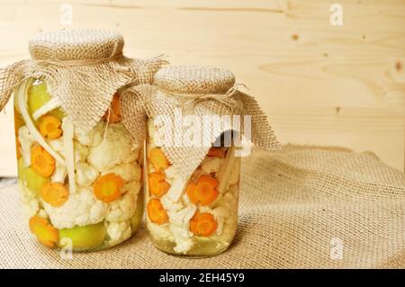 Konzept von zwei saisonalen Gurkenscheiben Glas mit farbigen grünen rohen Tomaten, orange Karotte und weißen Blumenkohl auf natürlichem Holzhintergrund. Vorderansicht Stockfoto