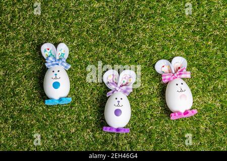 Traditionelles festliches Osterkonzept. Bunte niedliche handgemachte Kaninchen aus Eiern auf grünem Gras Hintergrund, Draufsicht Stockfoto