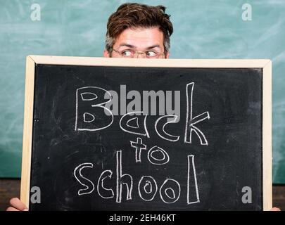 Lehrer oder Schulleiter begrüßt Inschrift zurück in die Schule. Lehrer heraus spähen Tafel. Erzieher versteckt sich hinter Tafel. Schulsachen kaufen. Vorbereitung auf die Schule. Sind Sie bereit, zu studieren. Stockfoto