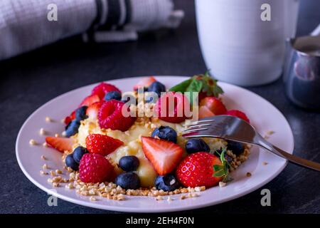 Protein-Mahlzeit mit hausgemachtem Vanillepudding, frischem Beerenmix und gerösteten Nüssen auf einem Teller auf dem Küchentisch. Stockfoto