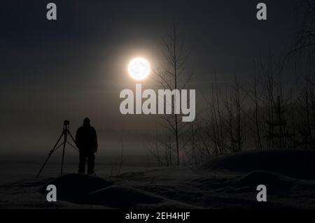 Fotograf steht im Schnee fotografiert Winterlandschaft. Vollmond und Sterne am Nachthimmel. Stockfoto