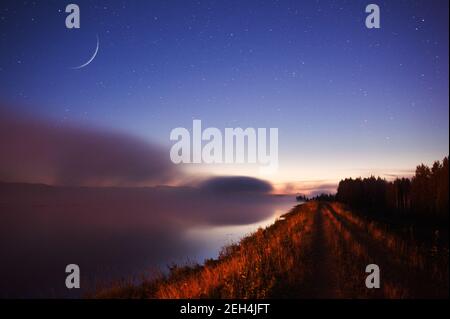 Wachender Halbmond über der nebligen Flusslandschaft. Stockfoto