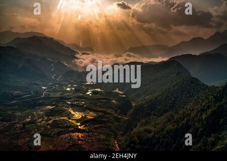 Weitläufige Reisfelder Luftaufnahme bei Sonnenaufgang. Dieser hat alles, Berge, Lichtstrahlen, Reflexionen, Sonnenaufgangsfarben, Reisfelder, dramatische Wolke Stockfoto