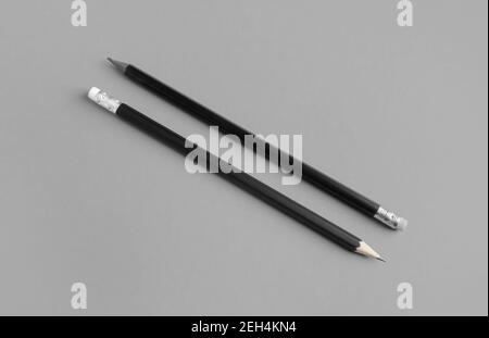 Zwei schwarze Bleistifte mit Kopierfläche auf grauem Papierhintergrund. Stockfoto