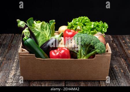 Bunte Gemüsekorb und gefüllt mit Brokkoli, Salat, Auberginen, Zwiebeln, Zucchini, Paprika und Kartoffeln. Auf einem hölzernen Hintergrund, Nahaufnahme. Stockfoto