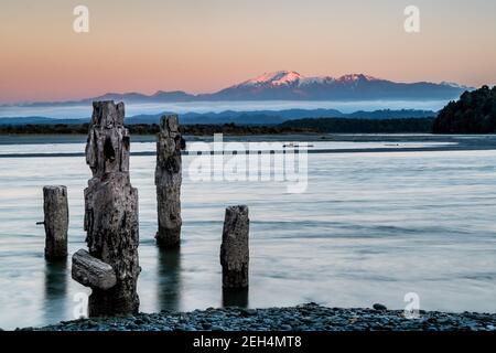 Langzeitbelichtung Sonnenaufgang mit Berghintergrund und verfallenen alten Dock Im Vordergrund alles in einem türkisblauen See Stockfoto