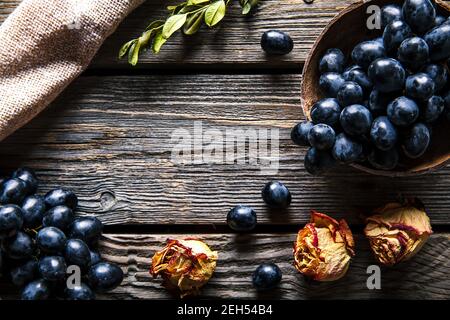 Trauben mit getrockneten Rosen auf Holzgrund. Obst, Blumen, Essen Stockfoto