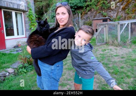 Frau hält schwarze Katze Mutter und Junge Sohn Kind suchen Bei der Kamera posieren Spaß machen dumme Gesichtsausdrücke draußen Im Garten UK KATHY DEWITT Stockfoto