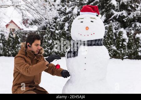 Ein Mann macht einen Schneemann in seinem Hof. Der Kerl freut sich im Winter und viel Schnee. Stockfoto