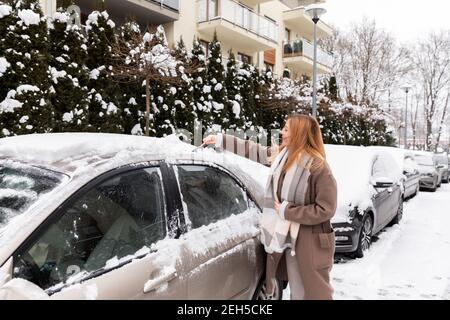 Eine junge Frau entfernt Schnee und Eis aus dem Auto. Stockfoto