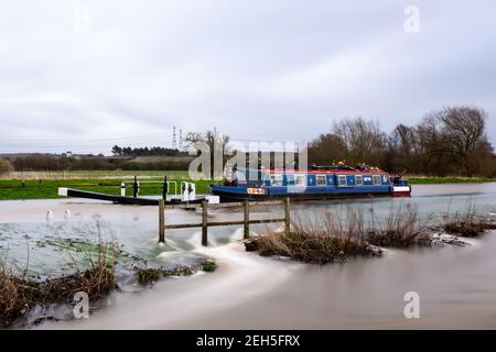Das Kanalboot steckte in einer überfluteten Schleuse mit hohem Fluss fest Mit Wasser fließt mit Geschwindigkeit in Felder und Schleppweg Bei Starkregen Unwetter Stockfoto