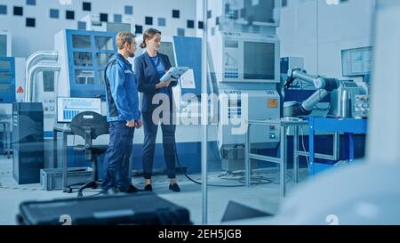 Fabrik-Workshop: Professionelle weibliche Ingenieur und männliche Maschinenbediener Verwenden Sie industriellen digitalen Tablet-Computer, um Roboterarm für die Produktion zu programmieren Stockfoto