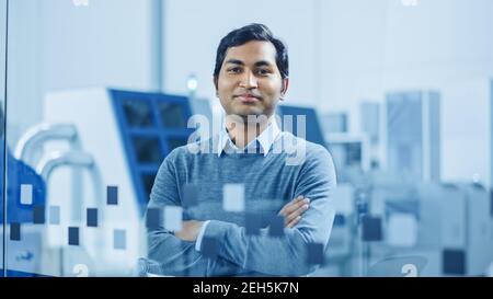 Modernes Fabrikbüro: Portrait eines gutaussehenden indischen Ingenieurs kreuzt Arme und Smiles charmant. Im Hintergrund High Tech Facility mit CNC Stockfoto