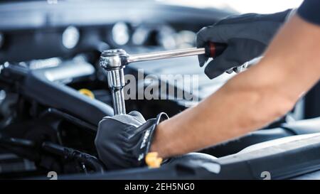 Nahaufnahme Aufnahme eines professionellen Mechaniks, der am Fahrzeug im Autodienst arbeitet. Motor Specialist Fixing Motor. Reparaturman trägt Handschuhe und verwendet einen Stockfoto