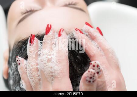Friseurhände waschen Haare der Brünette Frau mit Shampoo in speziellen Waschbecken für die Haarwäsche im Friseursalon. Stockfoto