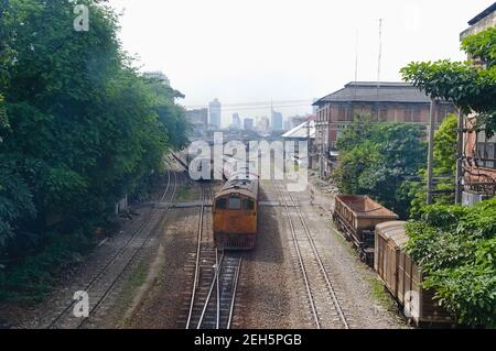 Lokomotive und Zug auf Eisenbahnschienen führt zu Bangkok Bahnhof Plattformen. Skyline der Stadt im Hintergrund. Bangkok, Thailand. Stockfoto