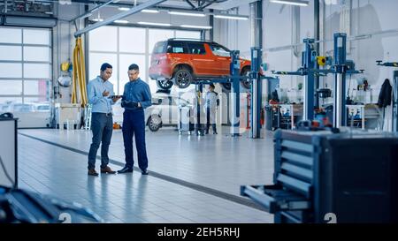 Manager prüft die Diagnoseergebnisse auf einem Tablet-Computer und erklärt einem Handsome Mechanic eine Fahrzeugpanne. Car Service-Mitarbeiter sprechen während Stockfoto