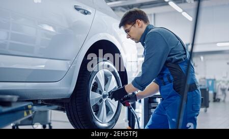 Mechaniker in blauen Overalls ist das Abschrauben von Schraubenmuttern mit einem pneumatischen Schlagschrauber. Der Reparaturdienst arbeitet in einem modernen Clean Car Service. Spezialisten Entfernt Stockfoto