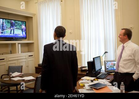 Präsident Barack Obama beobachtet seine Frau, First Lady Michelle Obama, im Fernsehen, während sie den Boden für den Gemüsegarten des Weißen Hauses bricht, 20. März 2009. Pressesprecher Robert Gibbs beobachtet mit ihm im Oberen Presseamt des Westflügels. Stockfoto