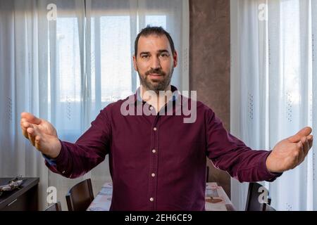 Schöner bärtiger Mann in einem lila Hemd mit offenen Armen wartet auf eine Umarmung. Freundschaftskonzept Stockfoto
