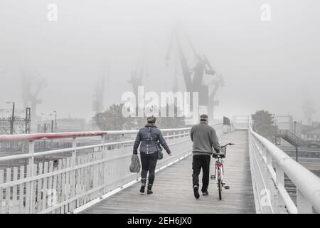 Blick auf zwei-Personen-Spaziergang auf der Fußgängerbrücke in der Werft in Danzig, Polen gegen einen nebligen Tag Stockfoto