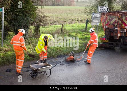 BUCKINGHAM, Großbritannien - 14. Dezember 2020. Straßenbauarbeiten, Team der Straßenbesatzung, Männer mit hoher Sichtbarkeit in orangefarbener Kleidung. Reparieren von Schlaglöchern in einem ländlichen Coun Stockfoto