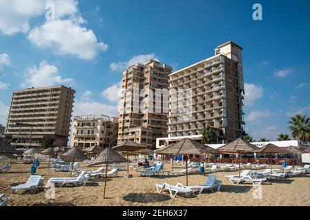 Palm Beach mit Sonnenschirmen und Touristen und verlassenen Hotels in Geisterstadt, Famagusta, Nordzypern Stockfoto