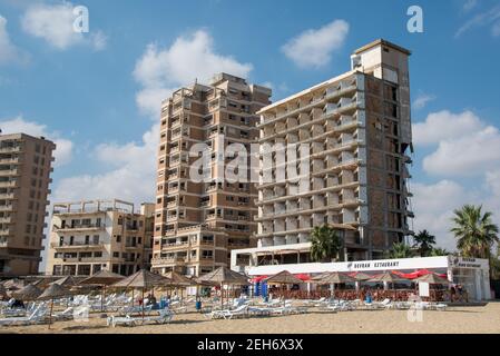 Palm Beach mit Sonnenschirmen und Touristen und verlassenen Hotels atghost Stadt, Famagusta, Nordzypern Stockfoto