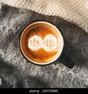 Draufsicht auf einen schwarzen Becher mit einem duftenden heißen Kaffee mit Zimt, auf dem das Symbol der Unendlichkeit gezeichnet ist. Abhängigkeit vom Kaffee. Der Morgen s Stockfoto