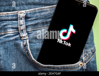TIK Tok Logo auf schwarzem Bildschirm des Smartphones in Jeans Tasche auf grünem Hintergrund Stockfoto