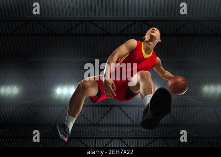 Junge professionelle Basketballspieler in Aktion, Bewegung isoliert auf schwarzem Hintergrund, Blick von unten. Konzept von Sport, Bewegung, Energie und dynamischen, gesunden Lebensstil. Training, Üben. Stockfoto