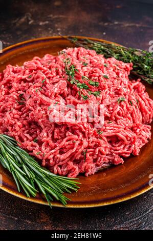 Rohes Hackfleisch oder Kalbfleisch auf einem rustikalen Teller mit Kräutern. Dunkler Hintergrund. Draufsicht Stockfoto