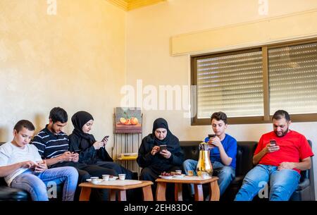 Arabische Familie sitzt zusammen, aber jeder von ihnen ist Am Telefon Stockfoto