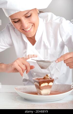 Der junge italienische Konditor legt Kakao auf eine Tasse Tiramisu Stockfoto