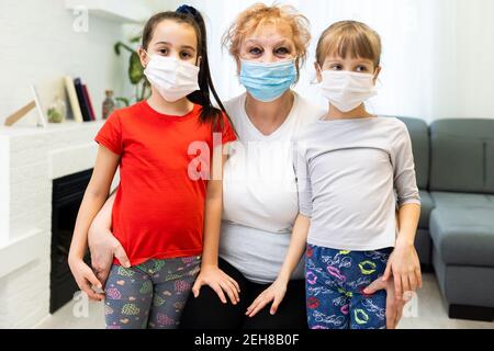 Großmutter und zwei Enkelinnen tragen medizinische Maske. Umarmung, einander trösten Stockfoto