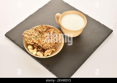 Mehrere ganze frische, duftende, köstliche Walnusskekse, mehrere natürliche Nüsse liegen auf einer keramischen leichten Untertasse, auf einer Servierplatte aus Schiefer. Stockfoto