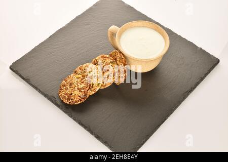 Mehrere ganze frische, duftende, köstliche Walnusskekse liegen auf einem Servierteller aus Schiefer, auf einem hellen Hintergrund, daneben ist eine leichte Keramikschale. Stockfoto