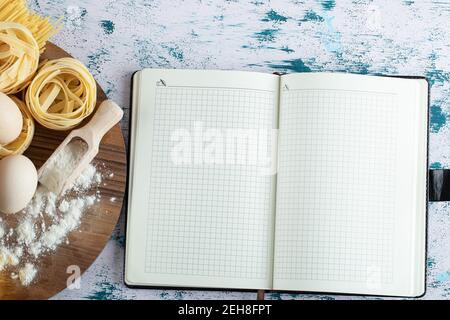 Tagliatelle mit Ei und Mehl auf Holzbrett und Notizbuch Stockfoto