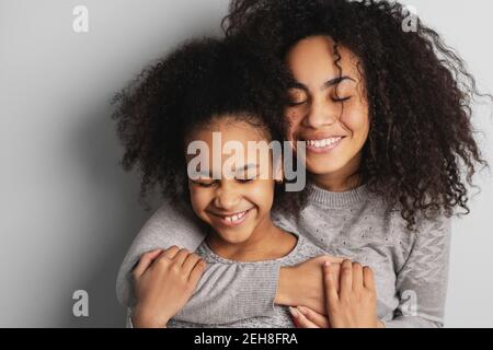 Happy african american Mama und ihre süße kleine Tochter lächeln und umarmen mit geschlossenen Augen. Stockfoto