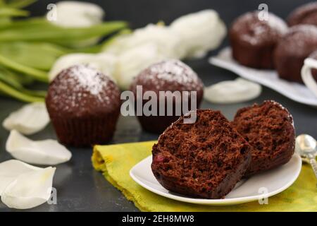 Schokoladen-Muffins mit Kirsche, bedeckt mit Puderzucker auf dunklem Hintergrund Stockfoto
