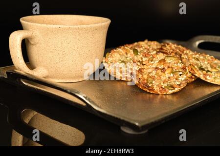 Mehrere ganze frische, duftende, köstliche Walnusskekse, auf einem Metalltablett, nächste ist eine Keramik-Tee-Tasse, auf einem schwarzen Hintergrund. Stockfoto